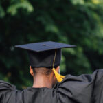 A student cheering in a graduation robe and hat, holding a diploma
