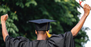 A student cheering in a graduation robe and hat, holding a diploma