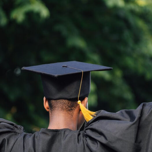 A student cheering in a graduation robe and hat, holding a diploma