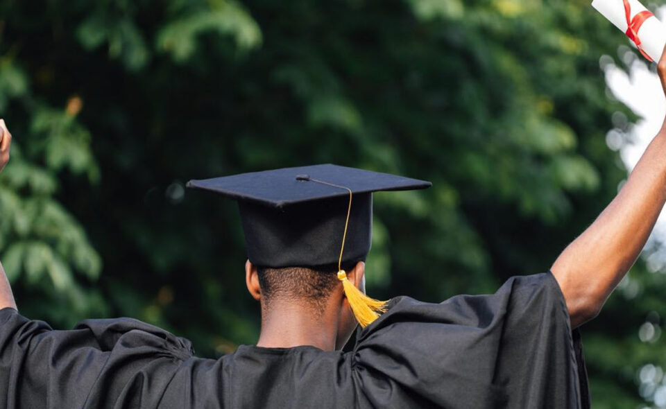 A student cheering in a graduation robe and hat, holding a diploma